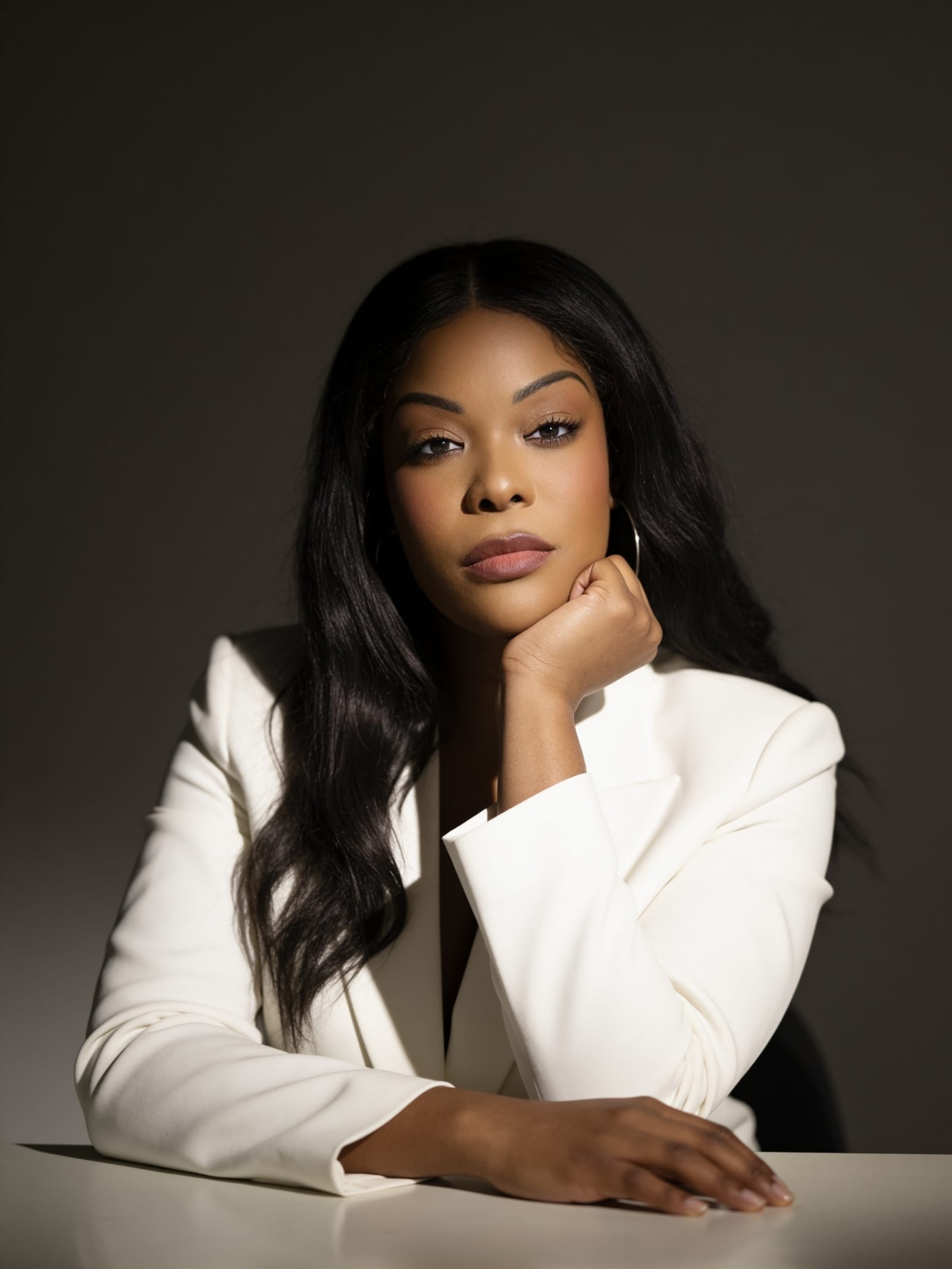 Calix Leigh-Reign in a white blazer, chin resting on her fist, against a warm neutral backdrop.